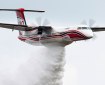 Red double-propeller airplane with black and red stripes drops water while airborne.