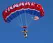 A person holds the toggles while descending to the ground underneath a red, white and blue parachute.
